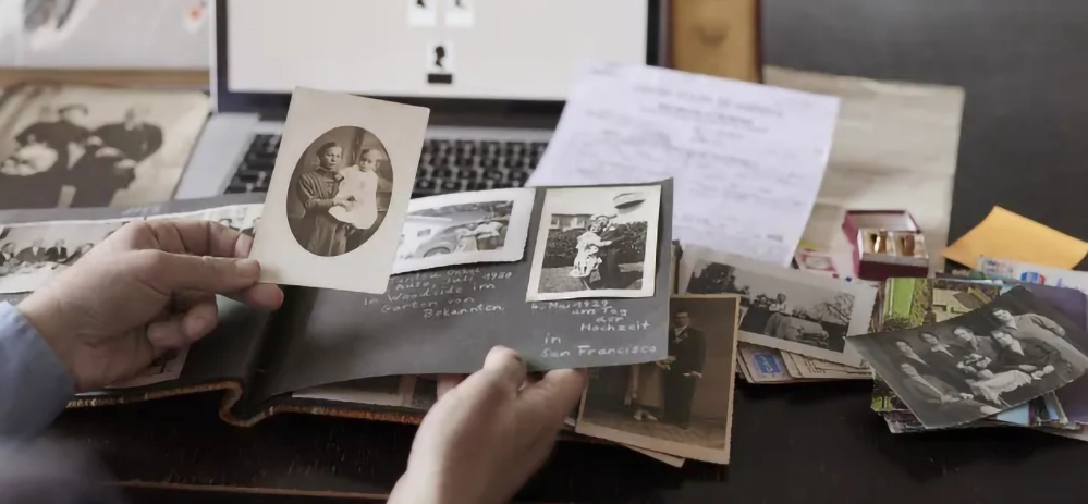 Hands sorting vintage family photographs on desk with laptop for digitizing old photos