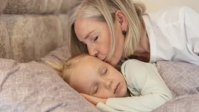 Grandmother kissing sick grandchild on forehead while child rests in bed