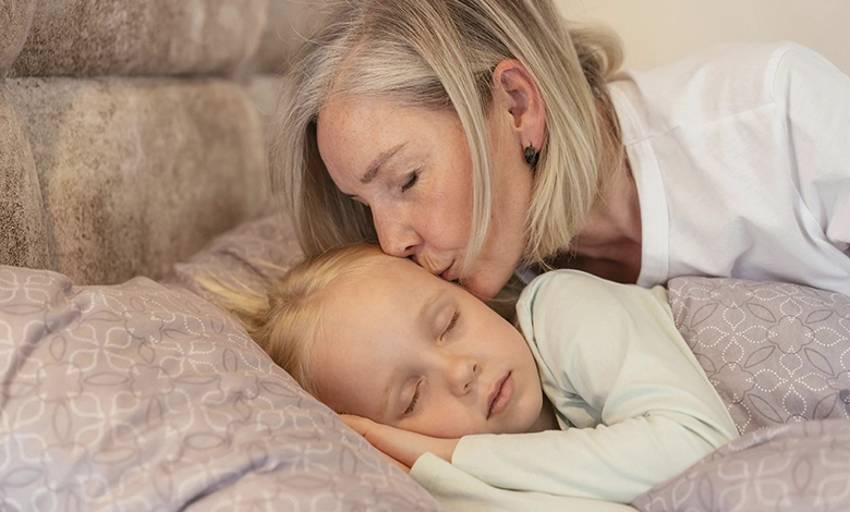 Grandmother kissing sick grandchild on forehead while child rests in bed