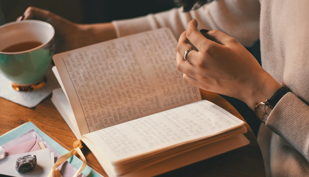 Woman writing in handwritten journal diary with coffee documenting family memories