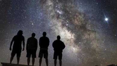 Four people standing in silhouette looking up at dramatic Milky Way galaxy in dark sky location