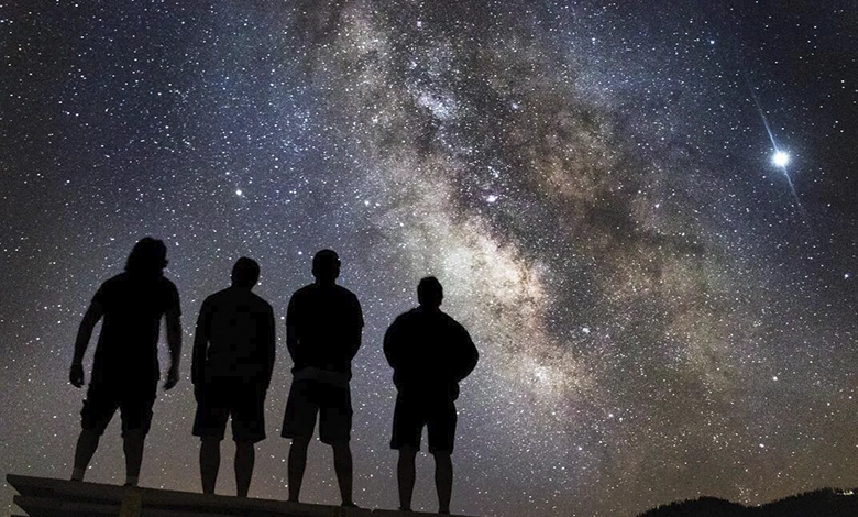 Four people standing in silhouette looking up at dramatic Milky Way galaxy in dark sky location
