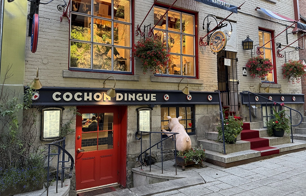 Whimsical pig statue outside Cochon Dingue restaurant with flower boxes and French signage in Old Québec City.