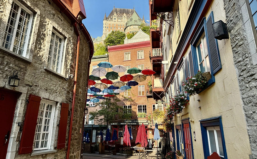 Rue du Cul-de-Sac in Old Québec City with colorful umbrellas, historic stone buildings, and Fairmont Le Château Frontenac in the background