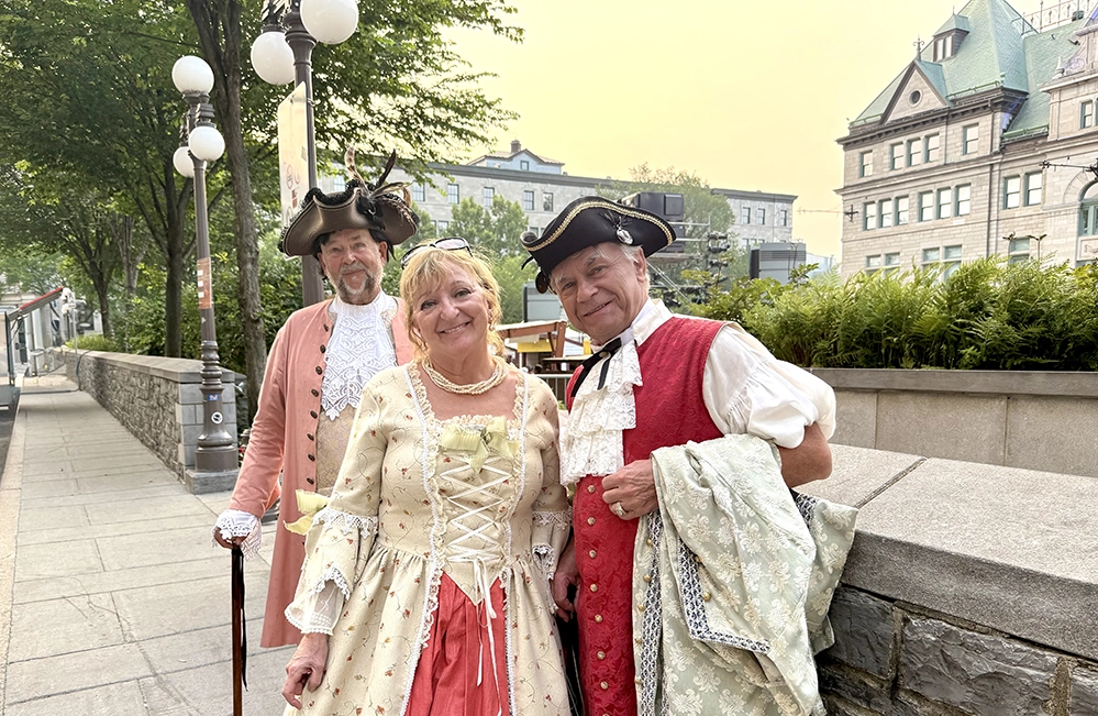 Three people in 18th century period costumes pose on stone steps during Québec City New France Festival in Old Town.