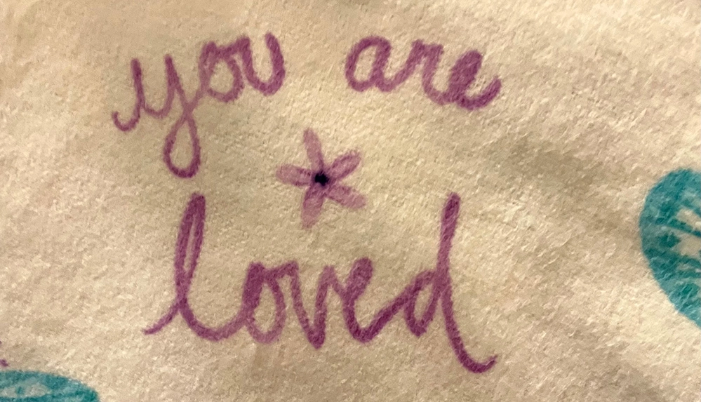 Handmade blanket with purple embroidered text 'you are loved' and butterfly designs from Sisters Sewing Kindness
