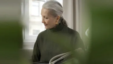 Woman with silver hair reading a book by a window as part of her self-care routine