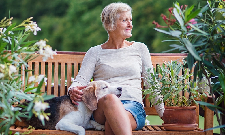 Senior woman relaxing on garden terrace with beagle resting beside her on bench