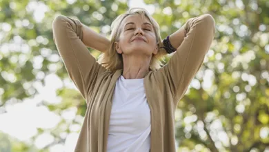 Woman with eyes closed and hands behind her head, relaxing outdoors in a sunlit park