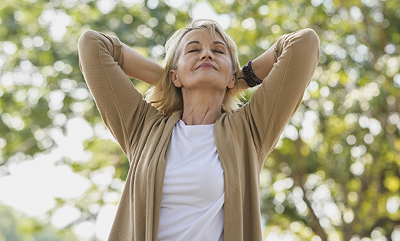 Woman with eyes closed and hands behind her head, relaxing outdoors in a sunlit park