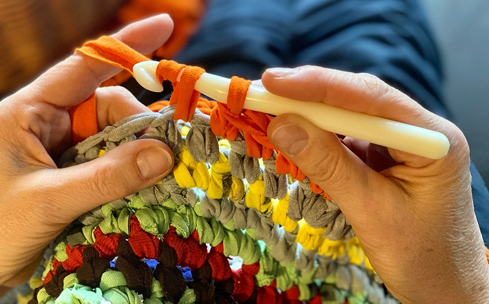 Close-up of hands crocheting colorful fabric with a white hook