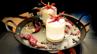 Fuego con Bourbon layered coffee cocktail in glass mugs with frothed milk, dried chili garnish, and coffee beans on a serving tray