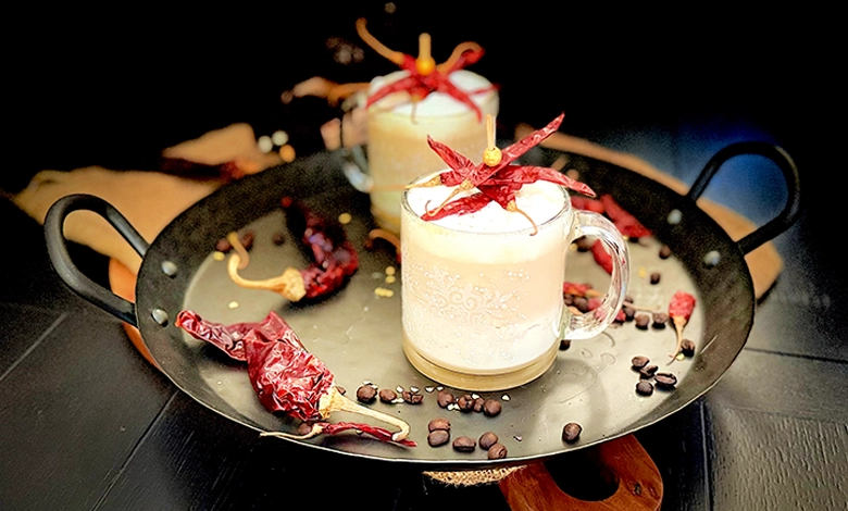 Fuego con Bourbon layered coffee cocktail in glass mugs with frothed milk, dried chili garnish, and coffee beans on a serving tray