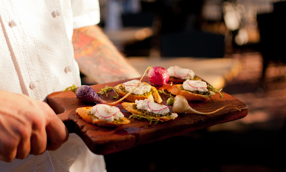 Scottsdale Winter Wellness: A Blue Zone-Inspired Desert Escape 4 Chef presenting artisan appetizers on a wooden board at The House Brasserie in Scottsdale with warm patio lighting