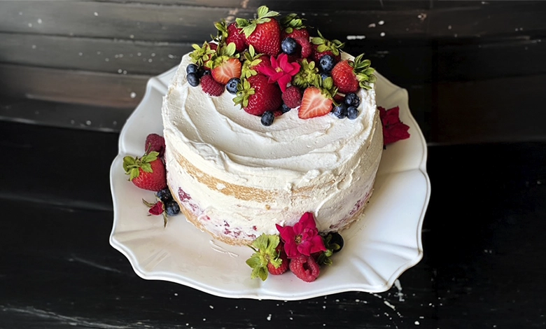 Strawberry angel food cake with mascarpone whipped cream topped with fresh strawberries, raspberries, blueberries, and pink flowers on a white scalloped plate