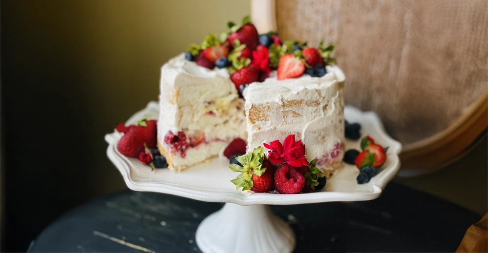 Sliced strawberry angel food cake showing layers of vanilla crème anglaise, fresh berries, and pink strawberry whipped cream