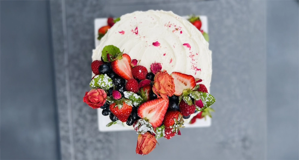 Overhead view of decorated strawberry angel food cake topped with fresh berries, dried roses, mint, and edible flower petals