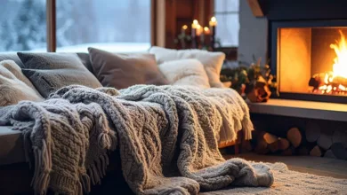 Cozy living room with knit throws on the sofa beside a glowing fireplace with a snowy view through the window