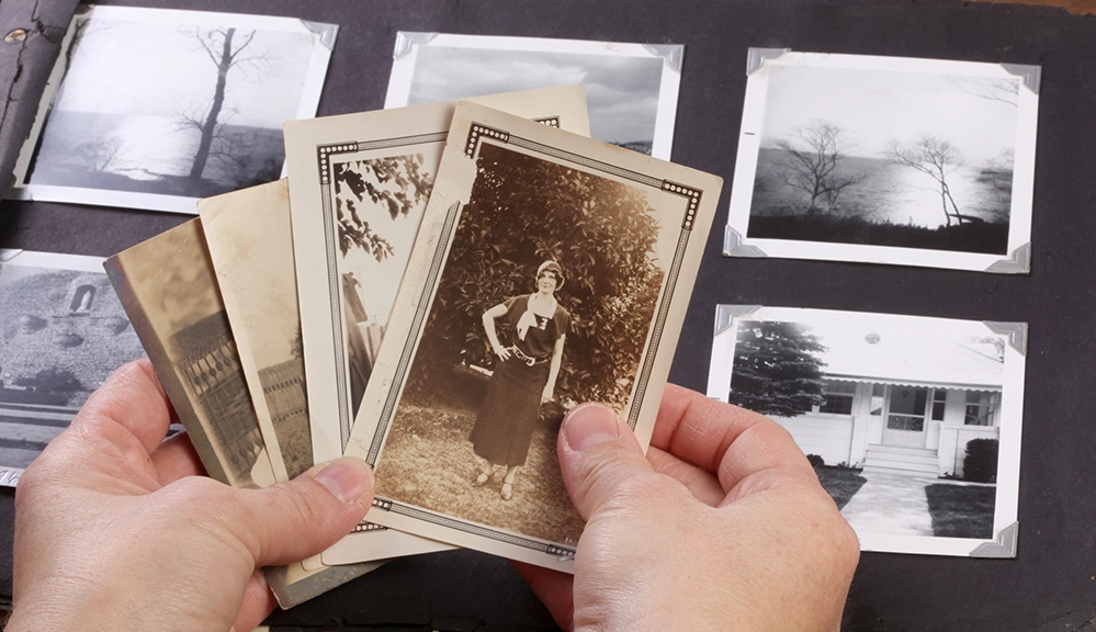 Hands holding vintage sepia photographs over an old family photo album