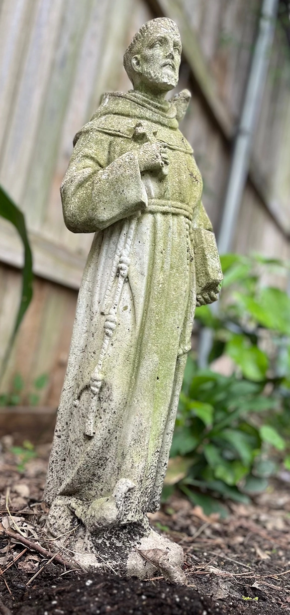 Weathered St. Francis garden statue standing in a flower bed