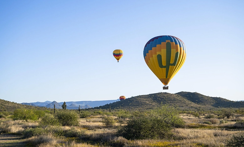 Colorful hot air balloons floating over Sonoran Desert landscape with saguaro cacti and desert hills