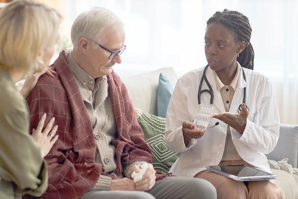 Black female doctor explaining medication to an elderly man while his adult daughter supports him at home