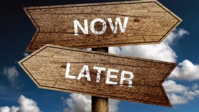 Wooden directional signs reading Now and Later pointing opposite directions against a blue sky