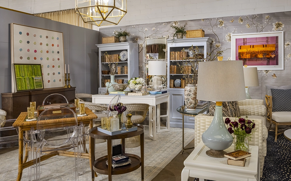 Bright airy designer vignette at The STUDIO Dallas by Studio Thomas James featuring ghost chairs, floral wallpaper, white bookcases, and eclectic art
