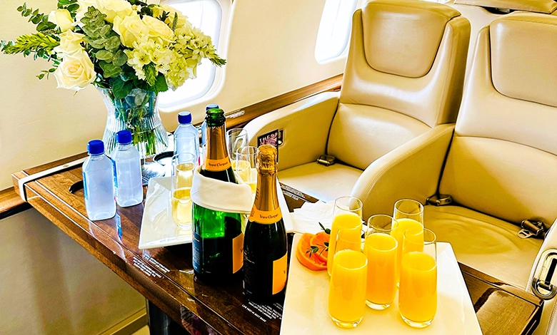 Champagne bottles, mimosas, and white roses on a table inside a Cirrus Aviation private jet cabin.