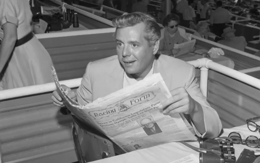 Desi Arnaz studying the Racing Form at the Del Mar Thoroughbred Club grandstands in 1957, surrounded by racetrack crowds