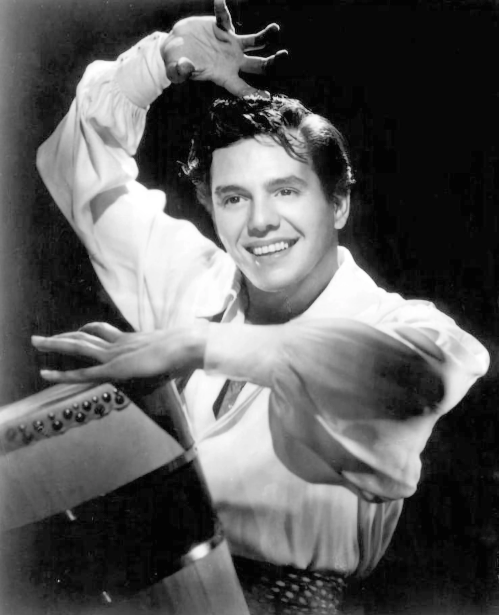 A young Desi Arnaz dancing and performing with exuberant energy in 1950, arms raised expressively