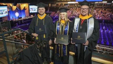 Tammy, Justin, and Mike France holding diplomas at graduation with service dog Skadi in a graduation gown