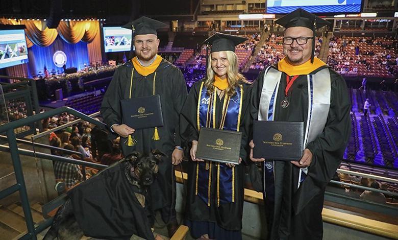 Tammy, Justin, and Mike France holding diplomas at graduation with service dog Skadi in a graduation gown