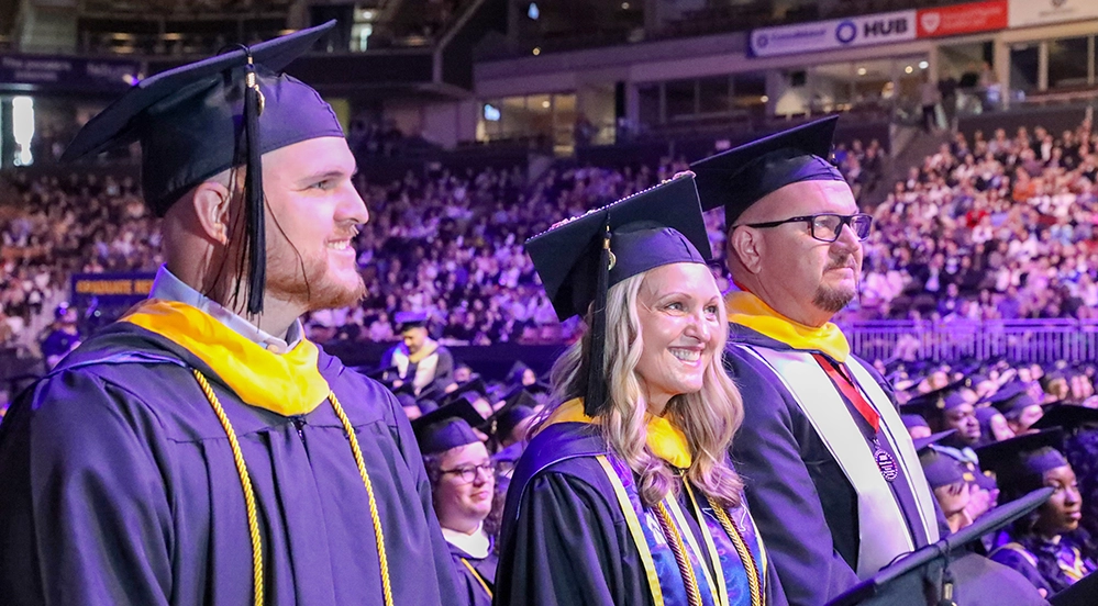 Justin, Tammy, and Mike France standing together in caps and gowns during SNHU commencement ceremony