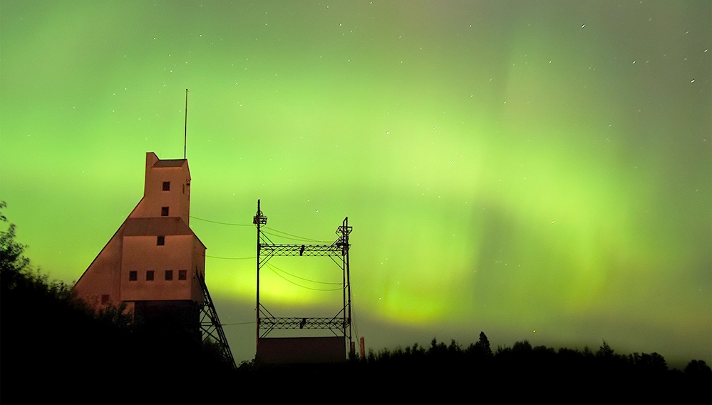 Historic Quincy Mine silhouetted against vivid green northern lights on Michigan’s Keweenaw Peninsula