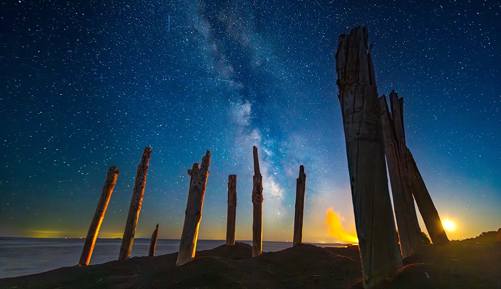 Weathered driftwood pillars silhouetted against the Milky Way galaxy over Lake Superior on Michigan’s Keweenaw Peninsula