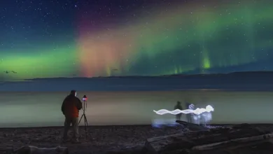 Photographer silhouetted against brilliant northern lights over Lake Superior on Michigan’s Keweenaw Peninsula, a dark-sky destination