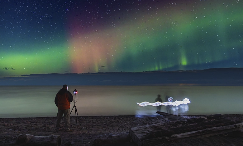 Photographer silhouetted against brilliant northern lights over Lake Superior on Michigan’s Keweenaw Peninsula, a dark-sky destination