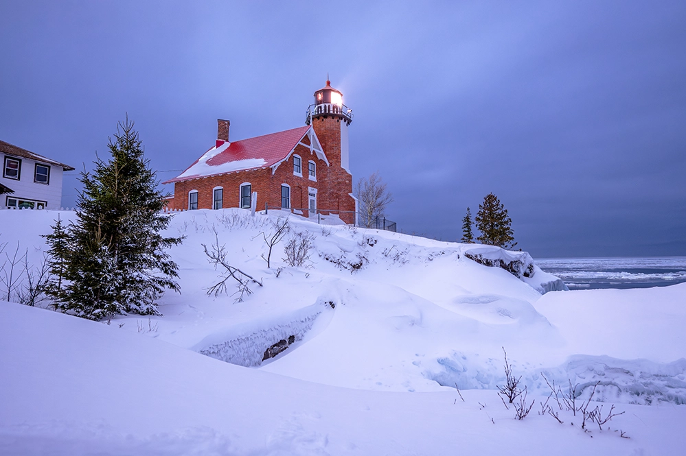 Eagle Harbor Lighthouse glowing at night in deep winter snow on Michigan’s Keweenaw Peninsula