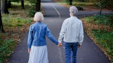 Older couple holding hands walking a tree-lined path from behind — dating after 60 and finding love again after loss