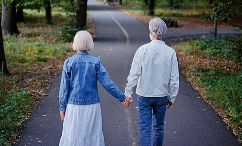 Older couple holding hands walking a tree-lined path from behind — dating after 60 and finding love again after loss