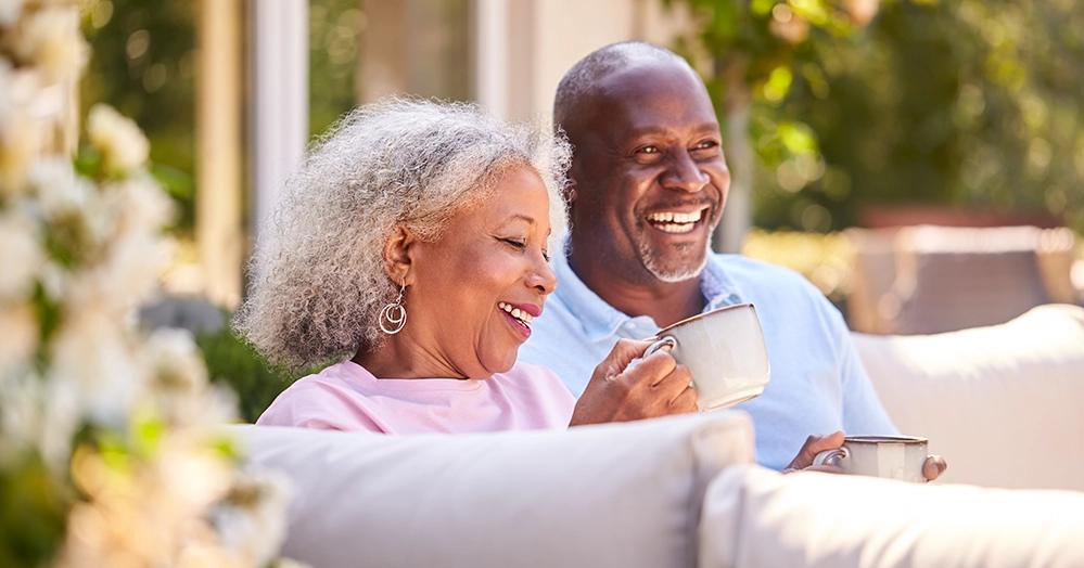 An older couple relaxes and laughs together outdoors over coffee, illustrating the everyday habits that support brain health and may reduce dementia risk.