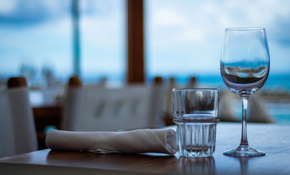 A 16-Day South Pacific Cruise: Stories and Lessons of Purpose, Passion, and Life 2 Wine glass and water glass on a set table beside a window with an ocean view on a cruise ship.