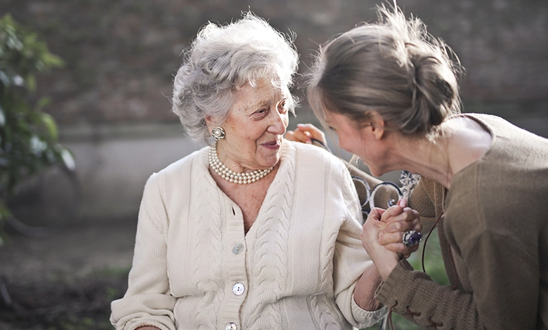 An older woman and her adult daughter hold hands and talk warmly outdoors, a picture of the connection at the heart of caring for aging parents.