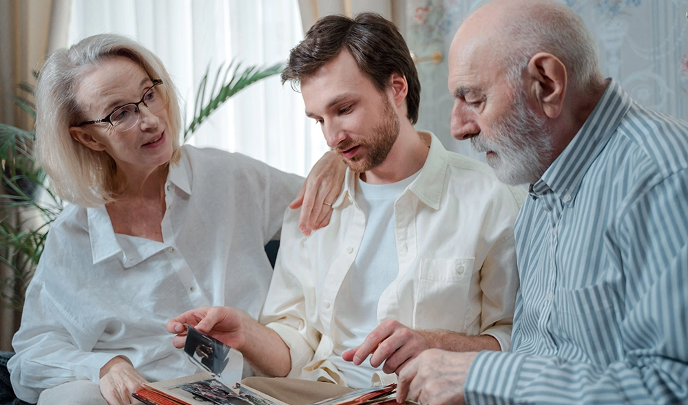 Caring for Aging Parents at Home: A Practical Guide for Adult Children 5 Three generations of a family look through a photo album together, a reminder that caring for aging parents works best as a team.