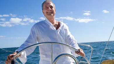 What’s Your Anchor in Retirement? 1 A smiling older man steering a sailboat on open water under a bright blue sky.