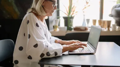 Woman in her sixties working at a laptop by a window at home