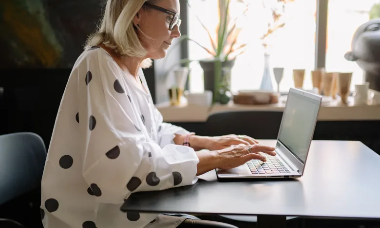 Woman in her sixties working at a laptop by a window at home