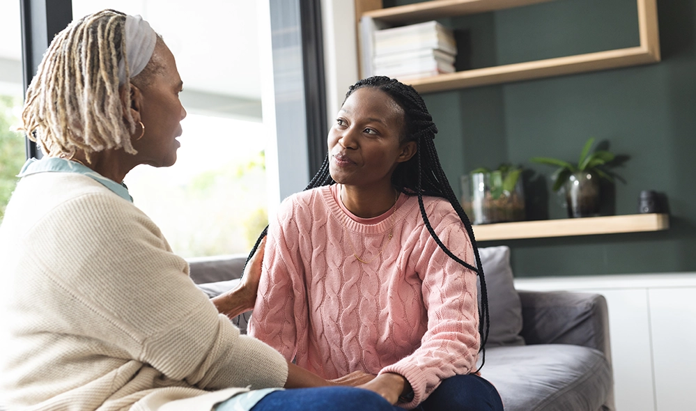Adult daughter sitting with her mother on a sofa, talking together