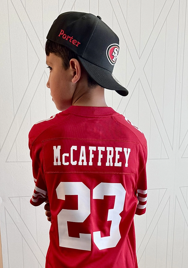 Boy from behind wearing a red San Francisco 49ers McCaffrey jersey and a black cap embroidered with his name